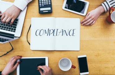 Compliance headline on paper notebook at small business office desk with young adult workers