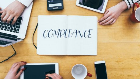 Compliance headline on paper notebook at small business office desk with young adult workers